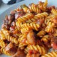 A plate of delicious sausage pasta mixed with Hot Fuzzz chilli sauce