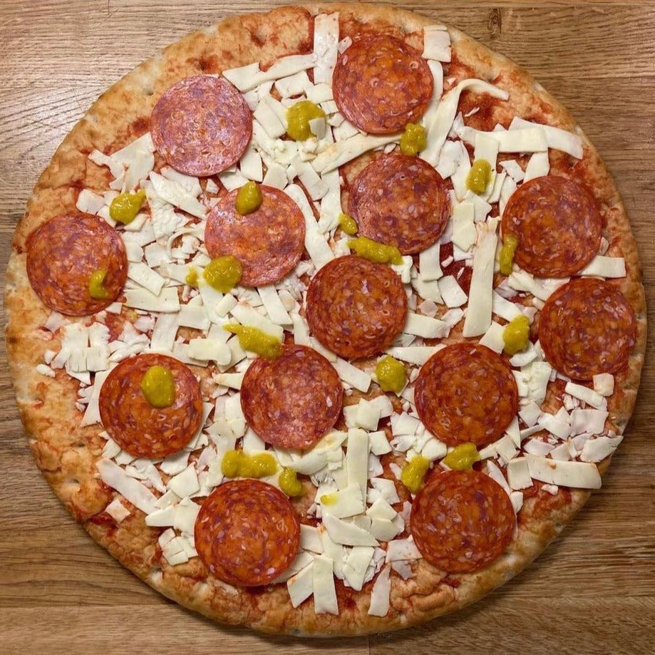 A fresh pizza before cooking drizzled with Renegade Mango hot sauce