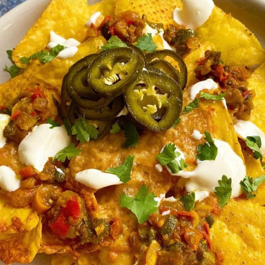 A picture of Nachos, smothered in Tasty Jalapeño, cheese, crème fraiche and sliced jalapeños